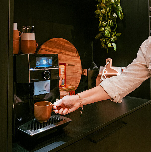 Hand neemt kopje koffie weg van Siemens volautomatische koffiemachine in zwarte keuken